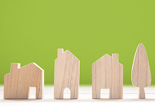 Bild mit grünem Hintergrund und drei Häusern und einem Baum aus Holz in Naturfarbe