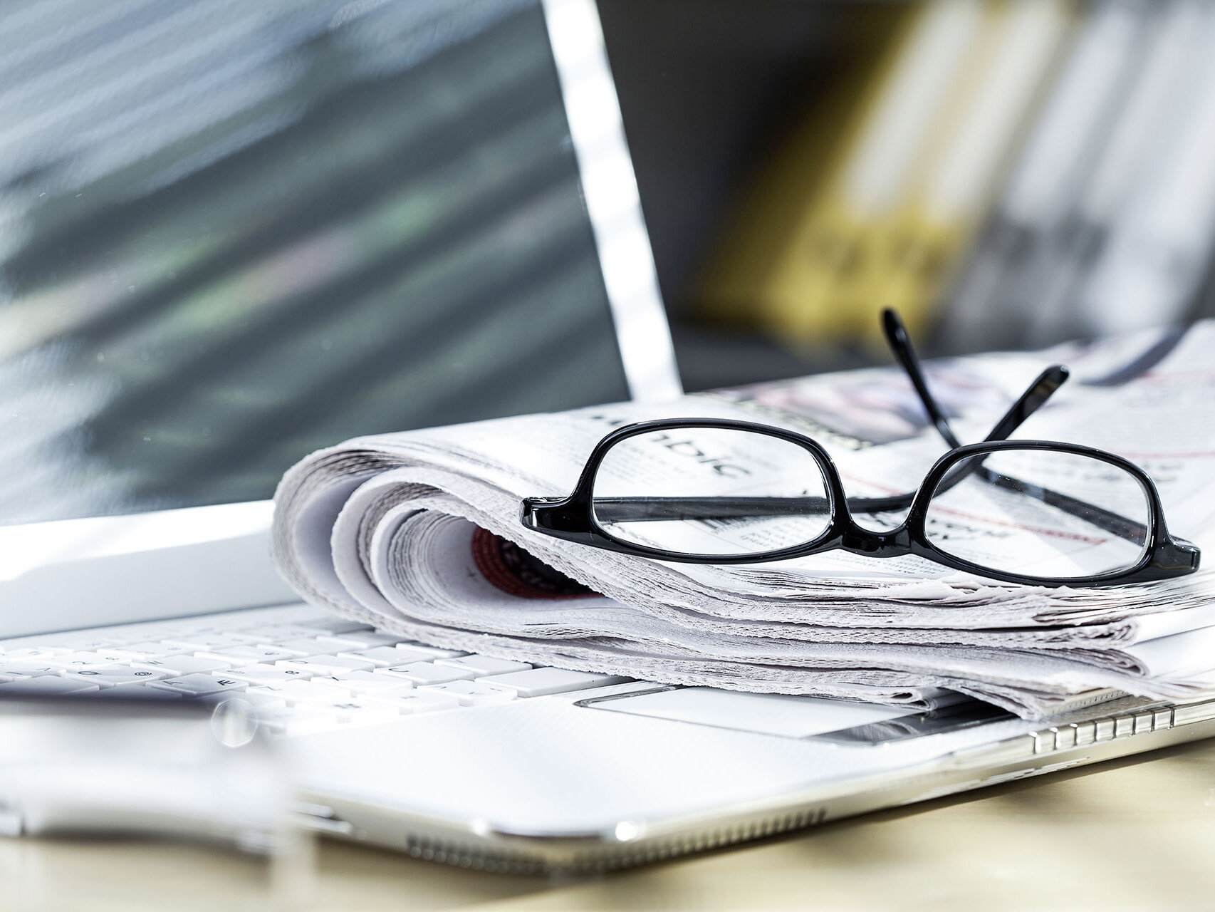 Eine Brille liegt auf einer Zeitung mit Laptop